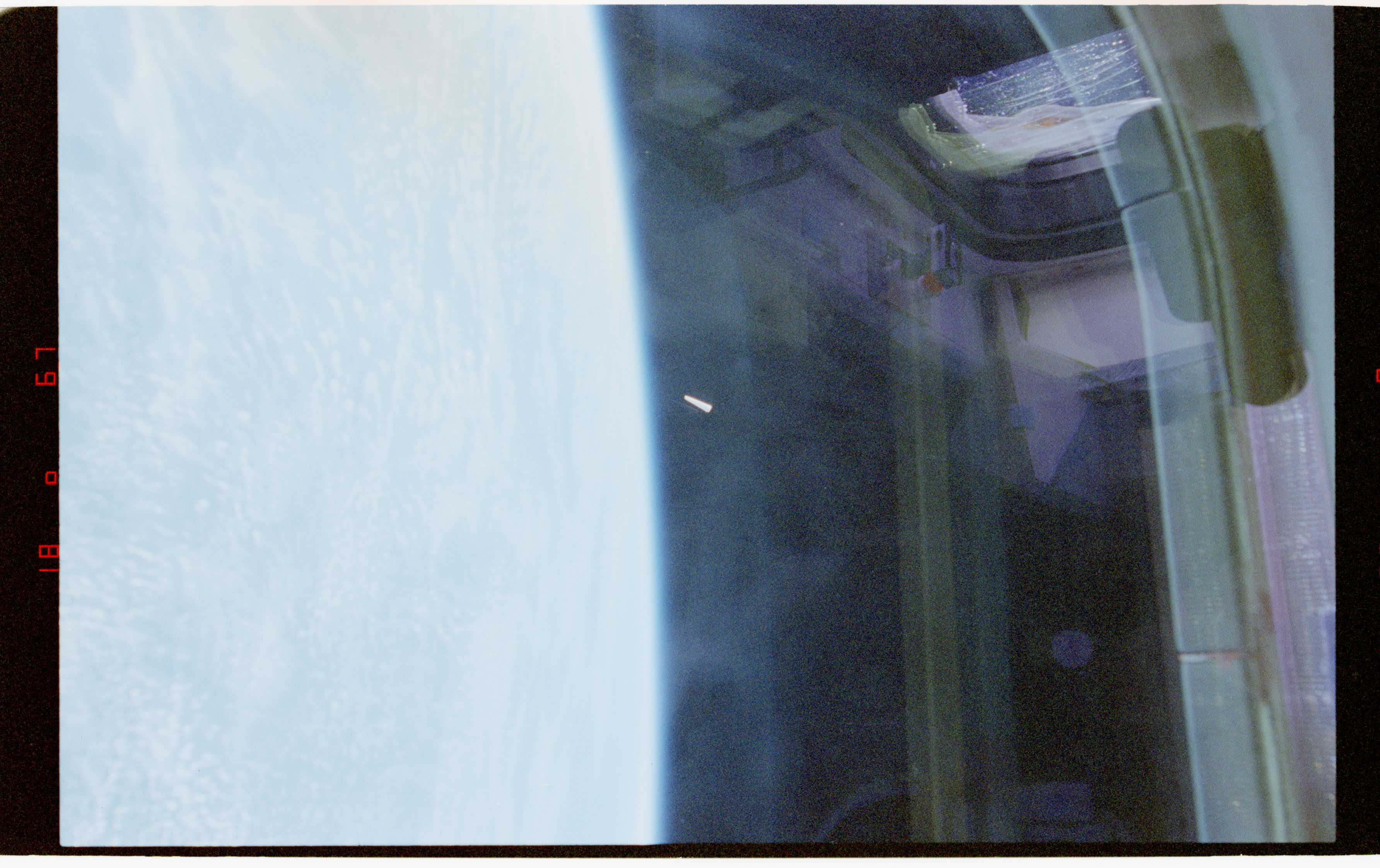 NASA STS-80 film frame (Nov-Dec 1996): a small bright elongated object against dark space near Earth's limb, photographed through Space Shuttle Columbia's window.