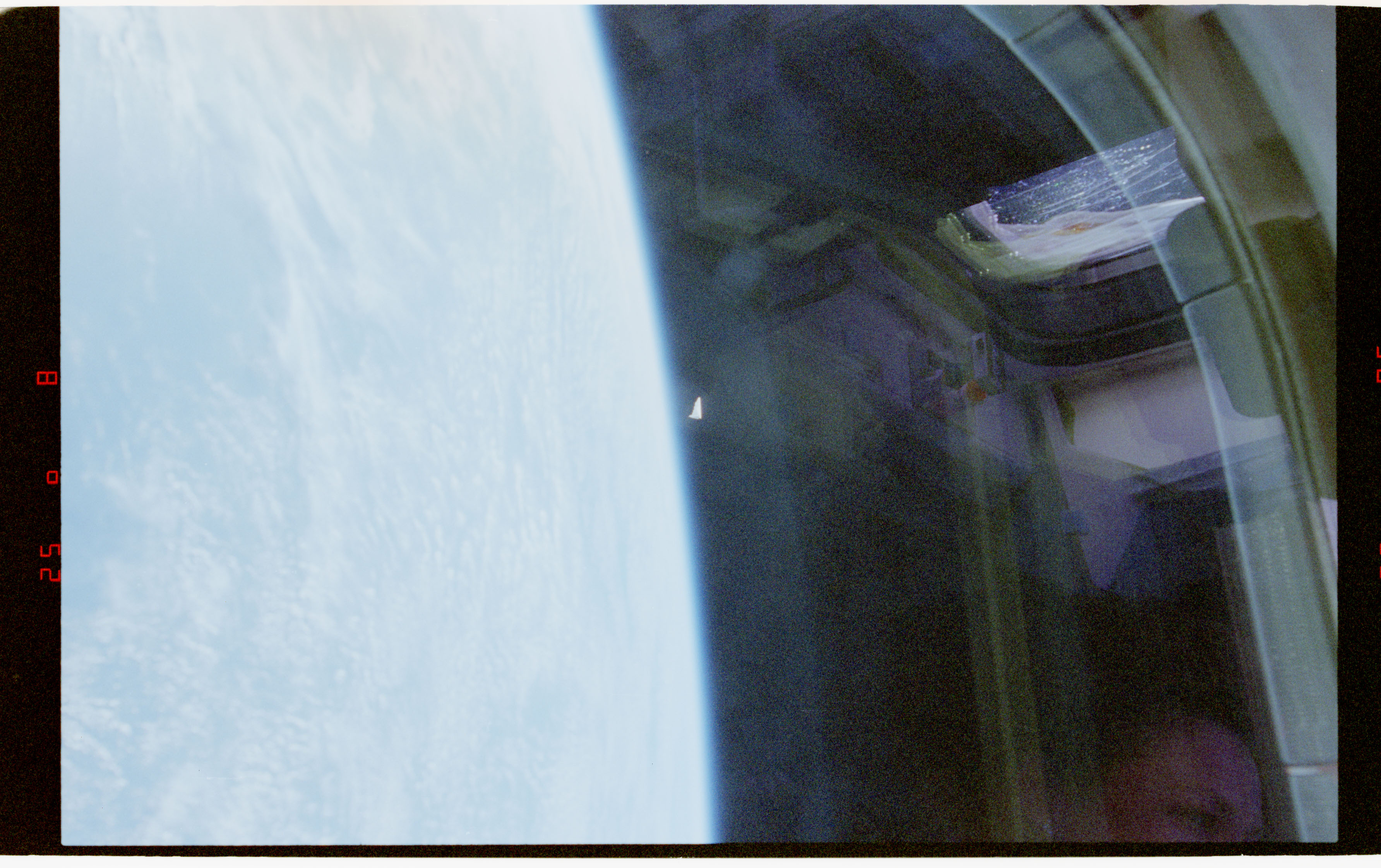 NASA STS-80 film frame (Nov-Dec 1996): a small bright conical object at the edge of Earth's limb, photographed through Space Shuttle Columbia's window.