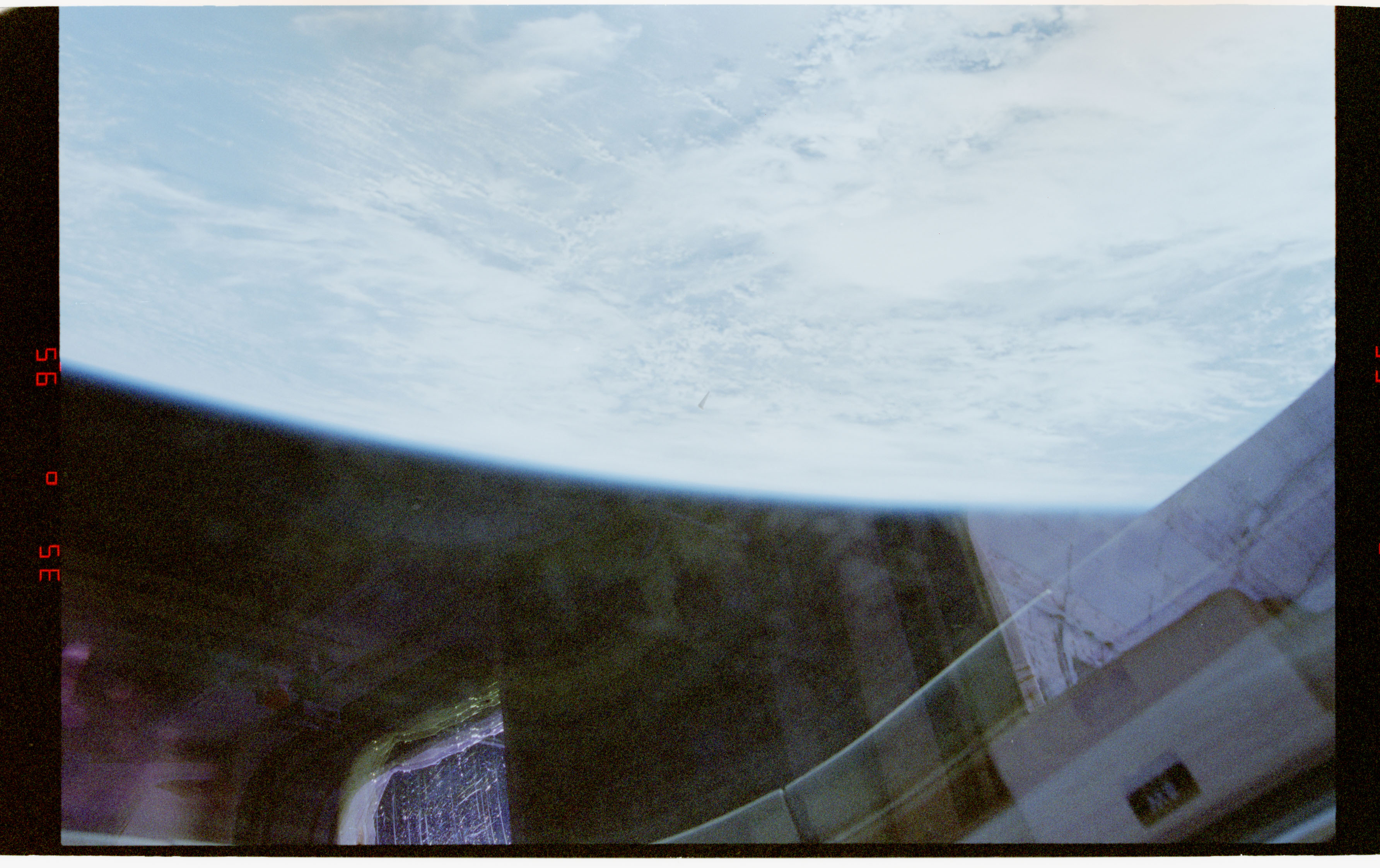 NASA STS-80 film frame (Nov-Dec 1996): a small dark triangular object against the cloud deck below, photographed from Space Shuttle Columbia.