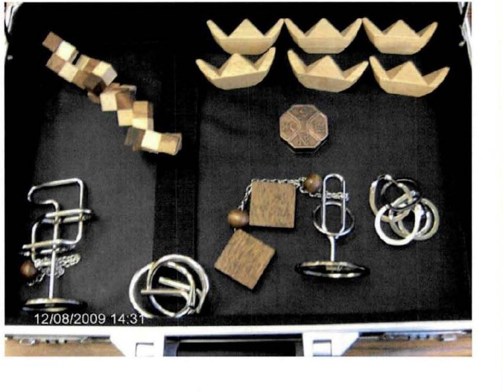 DOW-UAP-D173: an example series of BAASS "Tamper-Proof Games" -- wooden and wire brain-teaser puzzles laid out in an open briefcase, time-stamped 12/08/2009 14:31. BAASS assembled and photographed them in Las Vegas, locked the briefcases and placed them at a ranch "hotspot" for a month.